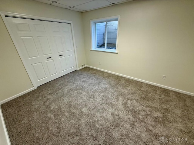 unfurnished bedroom with baseboards, a closet, dark carpet, and a drop ceiling