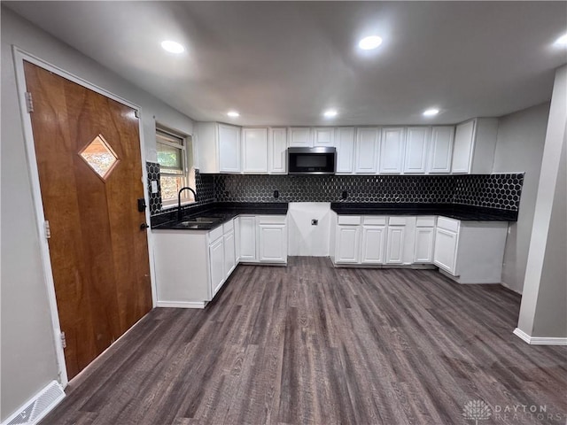 kitchen featuring dark wood-style flooring, a sink, white cabinets, backsplash, and stainless steel microwave