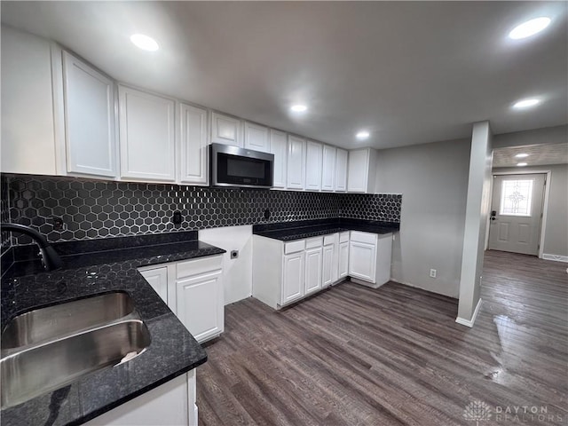 kitchen featuring white cabinets, dark stone counters, stainless steel microwave, dark wood-type flooring, and a sink