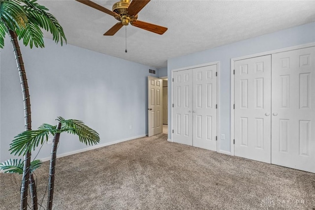 unfurnished bedroom featuring a textured ceiling, carpet floors, visible vents, baseboards, and two closets