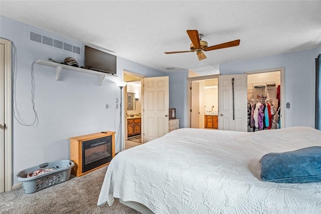 bedroom with ensuite bath, carpet, visible vents, and a walk in closet