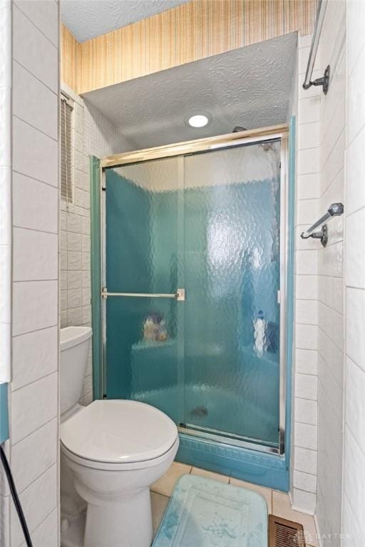 bathroom featuring a textured ceiling, tile patterned flooring, toilet, visible vents, and a shower stall