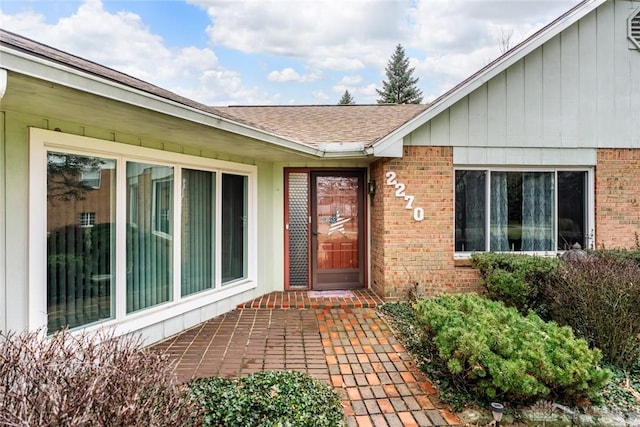 doorway to property featuring a shingled roof and brick siding