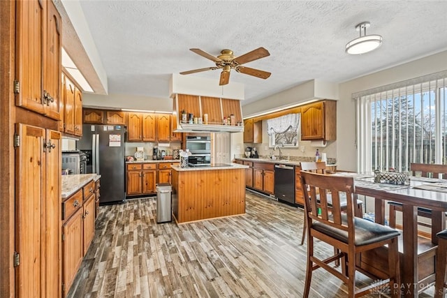 kitchen featuring appliances with stainless steel finishes, brown cabinets, light countertops, light wood-type flooring, and a sink