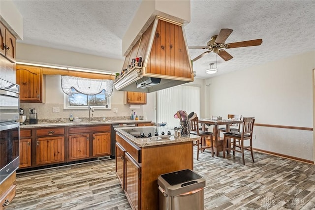 kitchen featuring light wood-type flooring, brown cabinets, a sink, and a textured ceiling