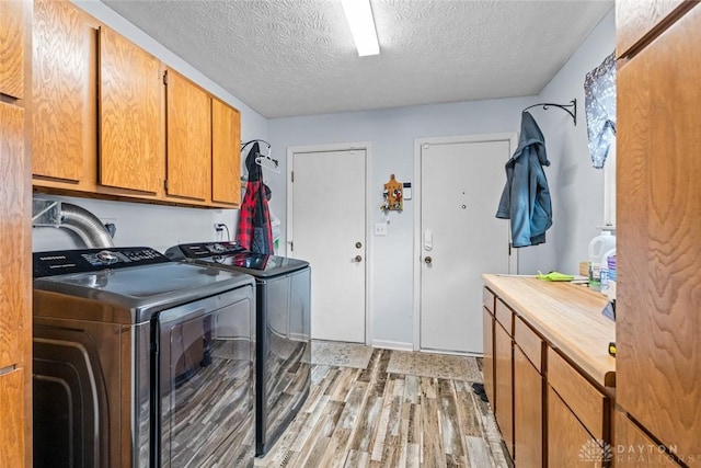 laundry room featuring light wood-type flooring, cabinet space, washer and clothes dryer, and a textured ceiling