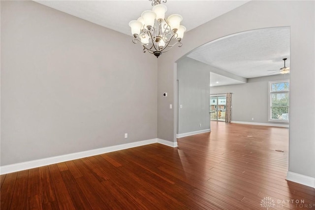 unfurnished room featuring arched walkways, ceiling fan with notable chandelier, wood finished floors, and baseboards