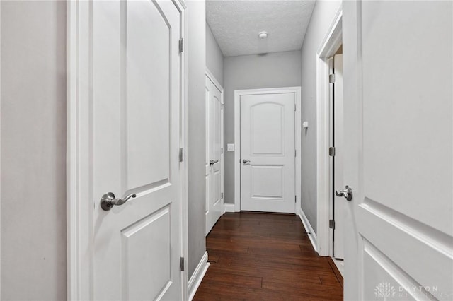 corridor with dark wood-style flooring, a textured ceiling, and baseboards