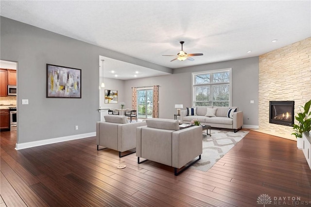 living room featuring ceiling fan, a fireplace, baseboards, and hardwood / wood-style flooring