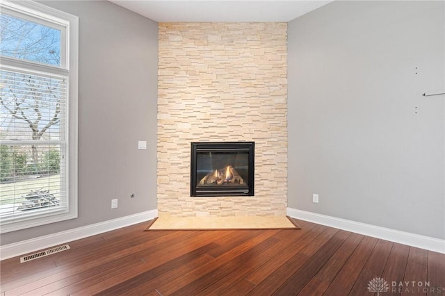 unfurnished living room with wood-type flooring, a fireplace, visible vents, and baseboards