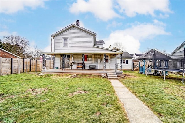 back of house featuring a trampoline, a yard, a chimney, a porch, and a fenced backyard