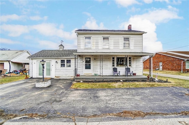 view of front facade featuring a porch, driveway, and a chimney