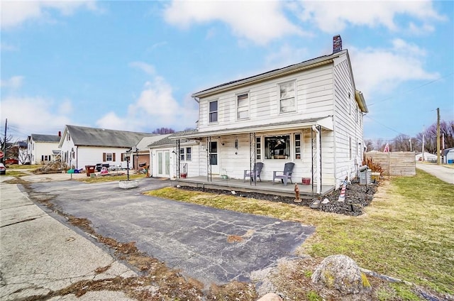 view of front of property featuring covered porch, a front lawn, and a chimney