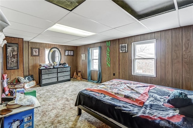 carpeted bedroom with wood walls and a paneled ceiling