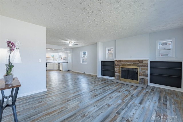 unfurnished living room with a textured ceiling, a stone fireplace, wood finished floors, and baseboards