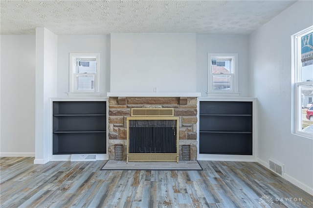 unfurnished living room with a textured ceiling, visible vents, and wood finished floors