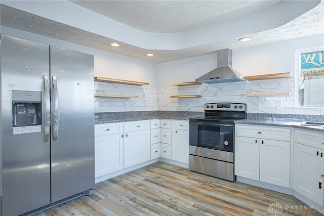 kitchen featuring light wood-style floors, stainless steel appliances, a textured ceiling, wall chimney range hood, and open shelves