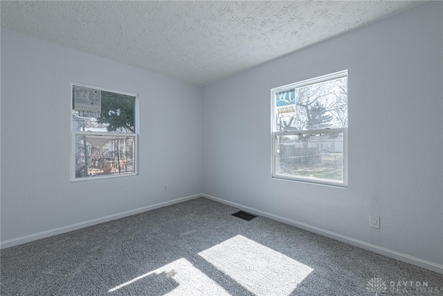 empty room featuring visible vents, carpet flooring, a textured ceiling, and baseboards