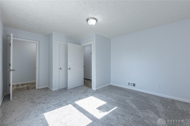 unfurnished bedroom featuring a textured ceiling, carpet flooring, visible vents, baseboards, and a closet