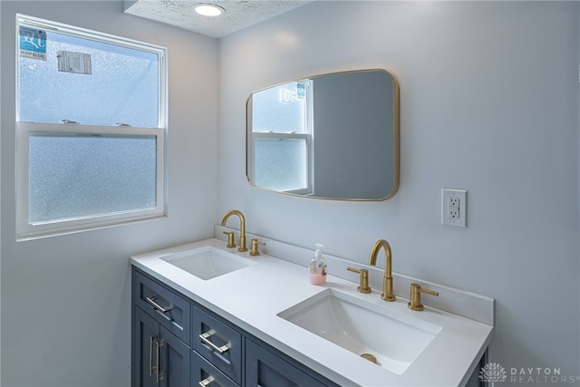 full bath with a sink, a textured ceiling, and double vanity