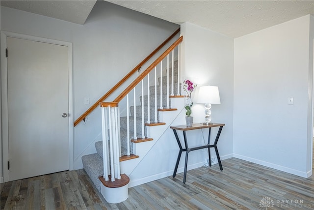 stairway with a textured ceiling, baseboards, and wood finished floors