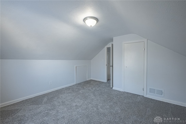 additional living space with a textured ceiling, lofted ceiling, carpet floors, visible vents, and baseboards