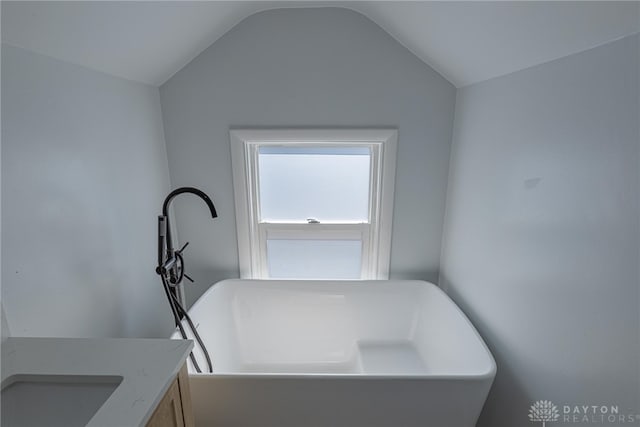 bathroom featuring a soaking tub, vaulted ceiling, and vanity