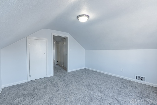 additional living space with a textured ceiling, lofted ceiling, carpet floors, visible vents, and baseboards