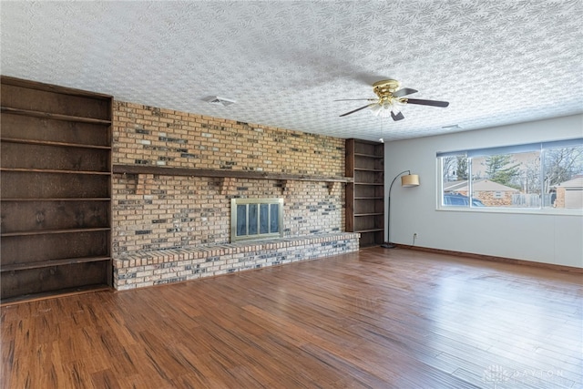 unfurnished living room with a textured ceiling, wood finished floors, baseboards, built in features, and a brick fireplace