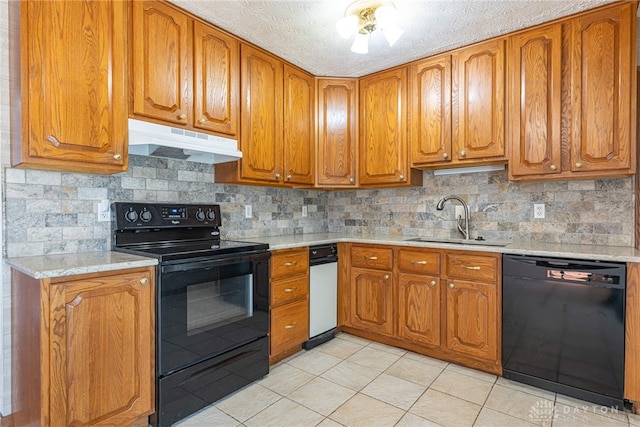 kitchen with brown cabinets, a sink, under cabinet range hood, and black appliances