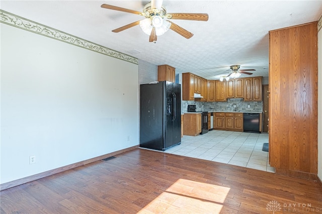 kitchen with light wood-style flooring, brown cabinets, light countertops, black appliances, and backsplash