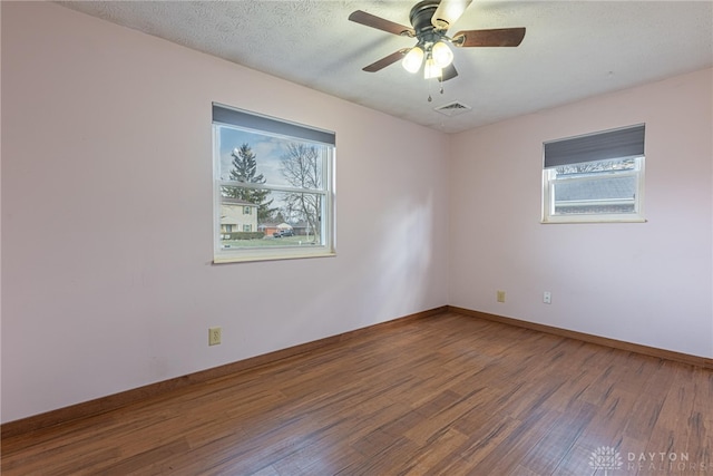 empty room with a textured ceiling, wood finished floors, a ceiling fan, visible vents, and baseboards