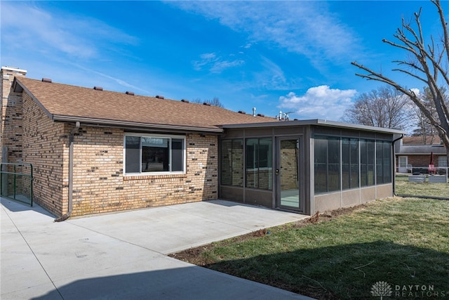 rear view of property featuring brick siding, a shingled roof, a lawn, a sunroom, and a patio area