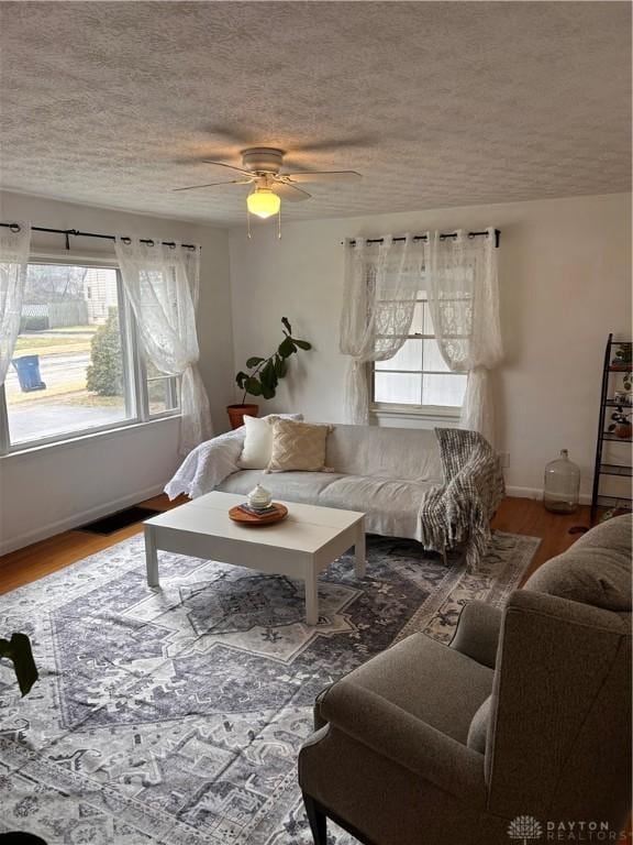 living area with a ceiling fan, a textured ceiling, baseboards, and wood finished floors