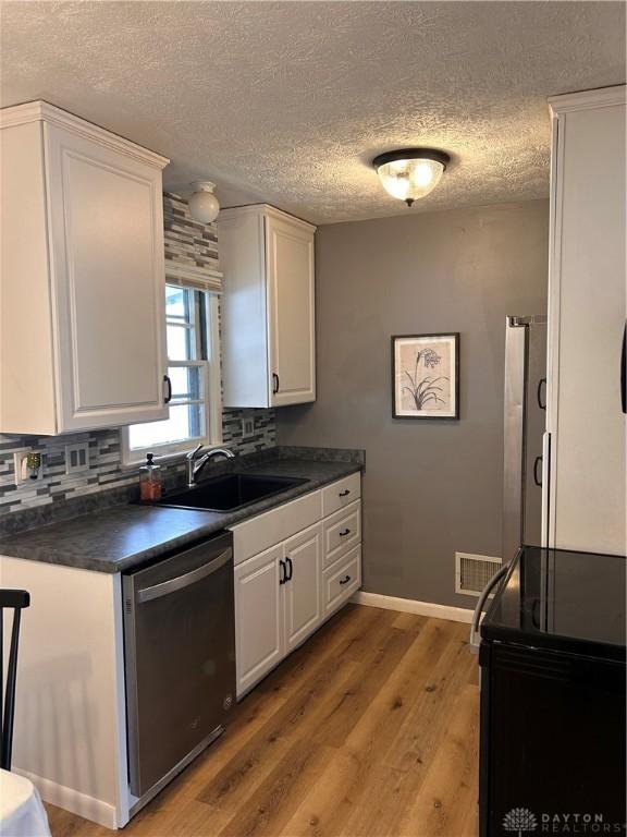 kitchen with dark countertops, appliances with stainless steel finishes, white cabinets, and a sink