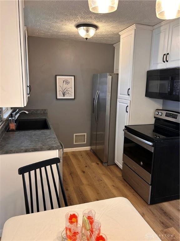 kitchen featuring visible vents, white cabinets, stainless steel appliances, light wood-type flooring, and a sink