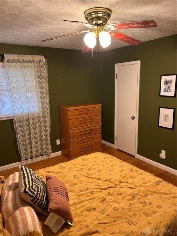 bedroom with ceiling fan, baseboards, a textured ceiling, and wood finished floors