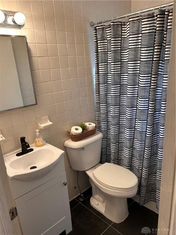 full bathroom with toilet, tile walls, vanity, and tile patterned floors