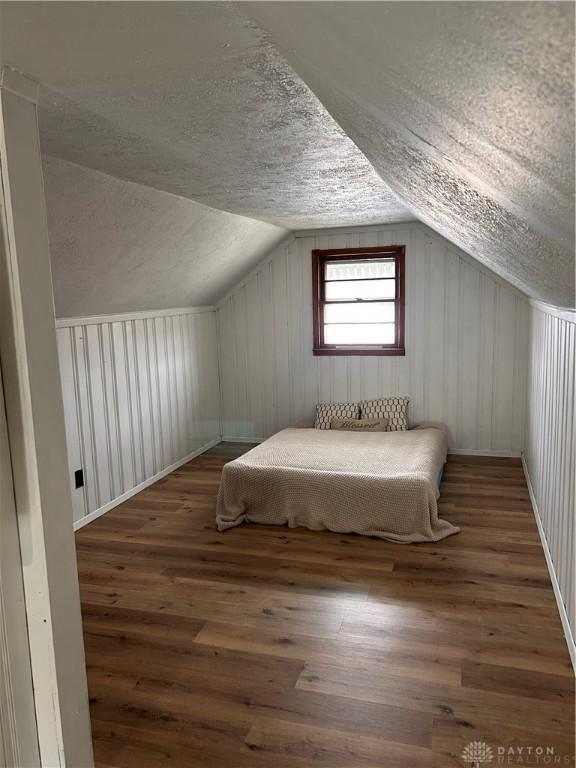 unfurnished bedroom with lofted ceiling, hardwood / wood-style flooring, and a textured ceiling