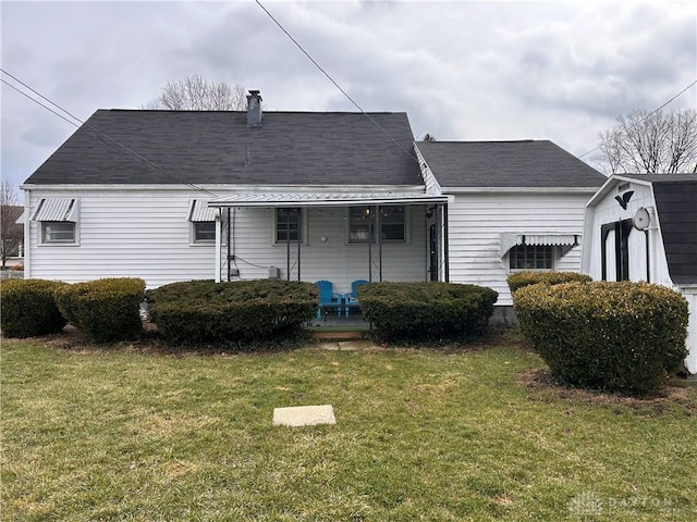 rear view of house with covered porch, a lawn, and roof with shingles