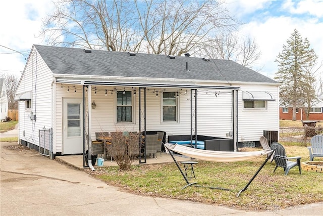 rear view of property featuring a fire pit, roof with shingles, a patio area, and fence