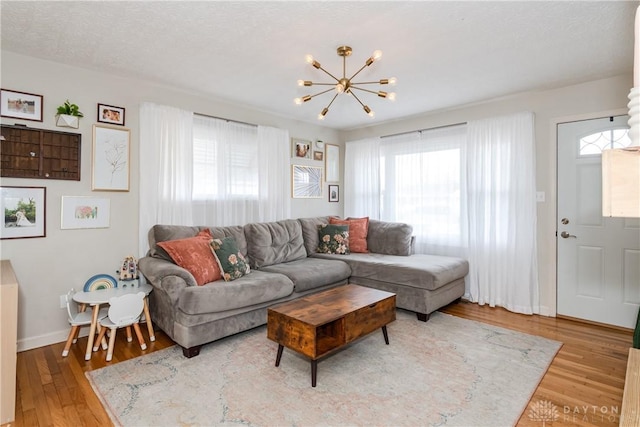 living room with baseboards, a textured ceiling, a chandelier, and wood finished floors