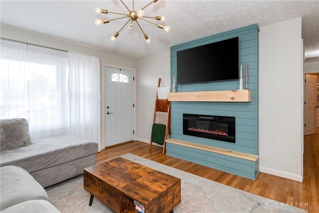 living room with a large fireplace, a textured ceiling, baseboards, and wood finished floors