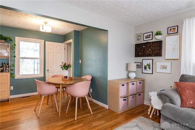 dining room with baseboards, light wood-style flooring, and a textured ceiling