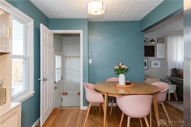 dining room featuring a textured ceiling, baseboards, a wealth of natural light, and light wood-style floors