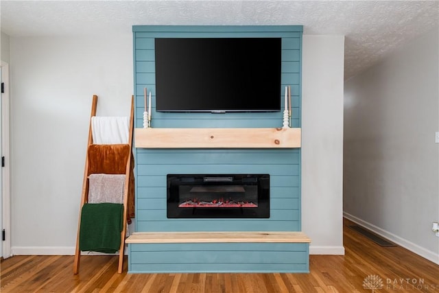 interior details featuring a textured ceiling, a fireplace, wood finished floors, visible vents, and baseboards