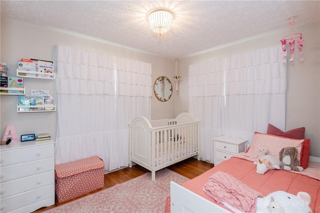 bedroom featuring a crib, a textured ceiling, and wood finished floors