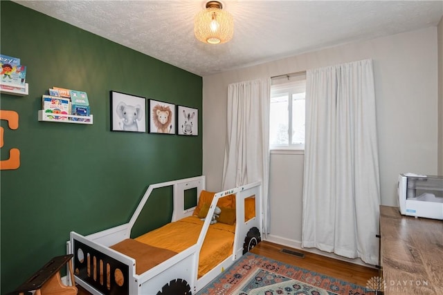 bedroom with a textured ceiling, visible vents, and wood finished floors