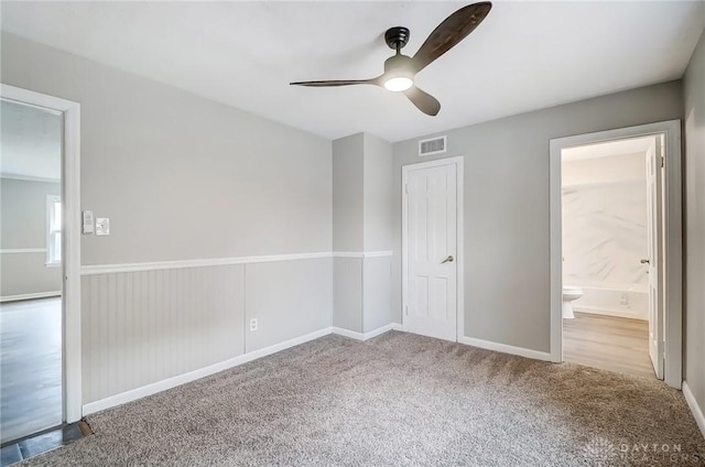 unfurnished bedroom featuring carpet floors, visible vents, ceiling fan, ensuite bath, and baseboards