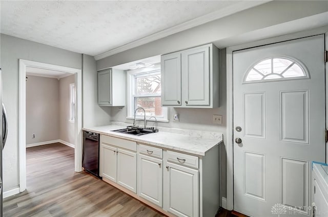 kitchen with a sink, baseboards, black dishwasher, light countertops, and light wood-style floors